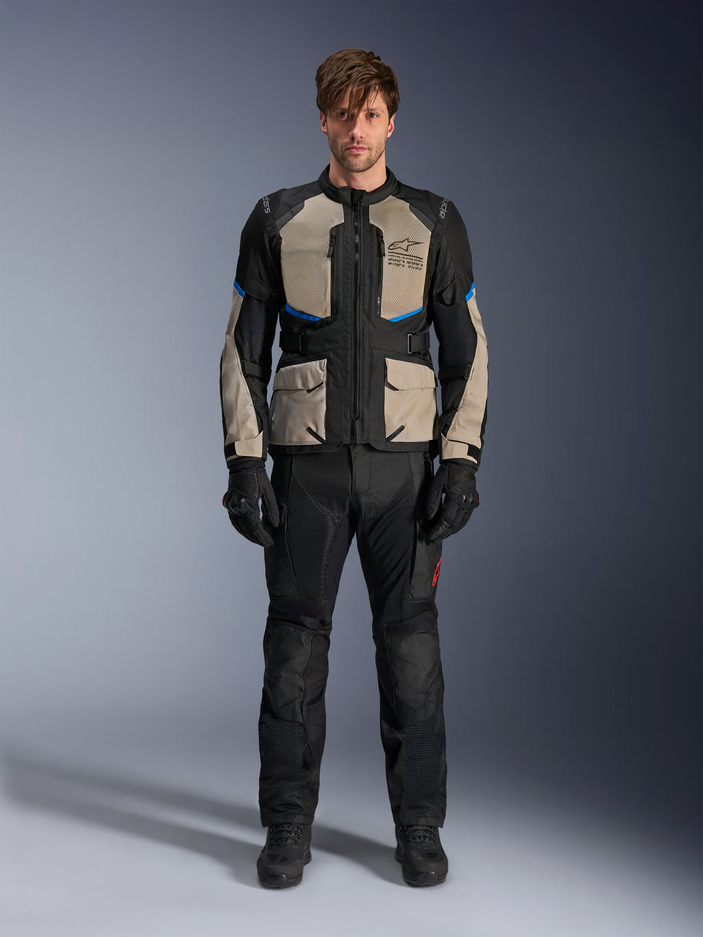 Modello che indossa la giacca Alpinestars Andes Air Drystar®, giacca da moto touring, colore Black Laurel Gray e Bright Blue, abbinata a pantaloni e guanti da guida neri coordinati, con ampi pannelli di ventilazione in mesh su petto e maniche per l'adventure touring in climi caldi.