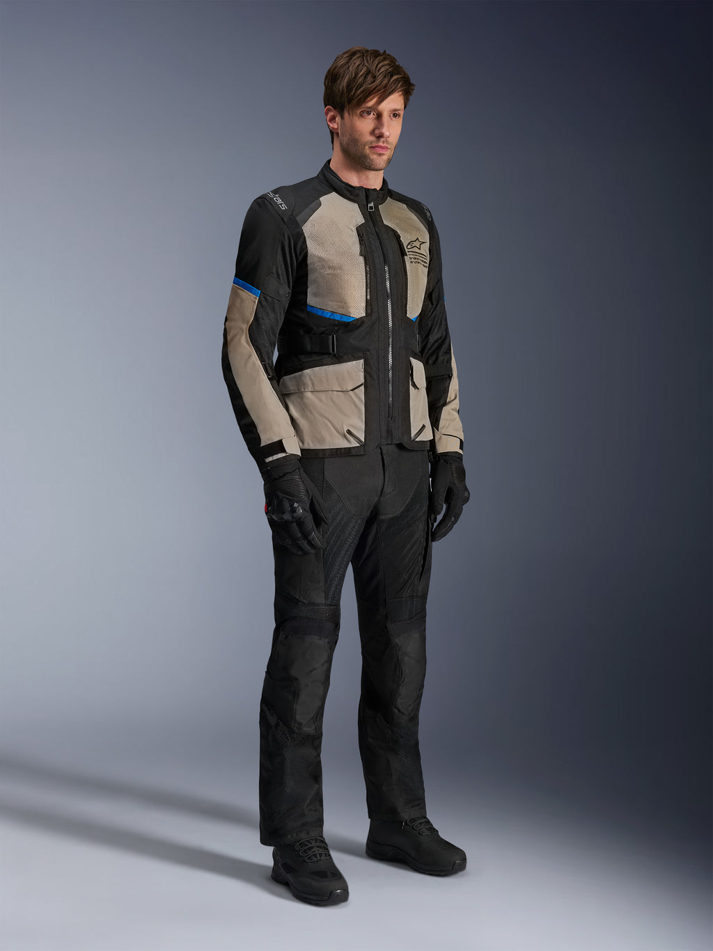 Giacca Alpinestars Andes Air Drystar®, giacca da moto touring, nero, grigio alloro e blu brillante, indossata con pantaloni e guanti da guida coordinati, dotata di ampi pannelli in rete per il flusso d'aria e vestibilità orientata alla strada, equipaggiamento adventure touring