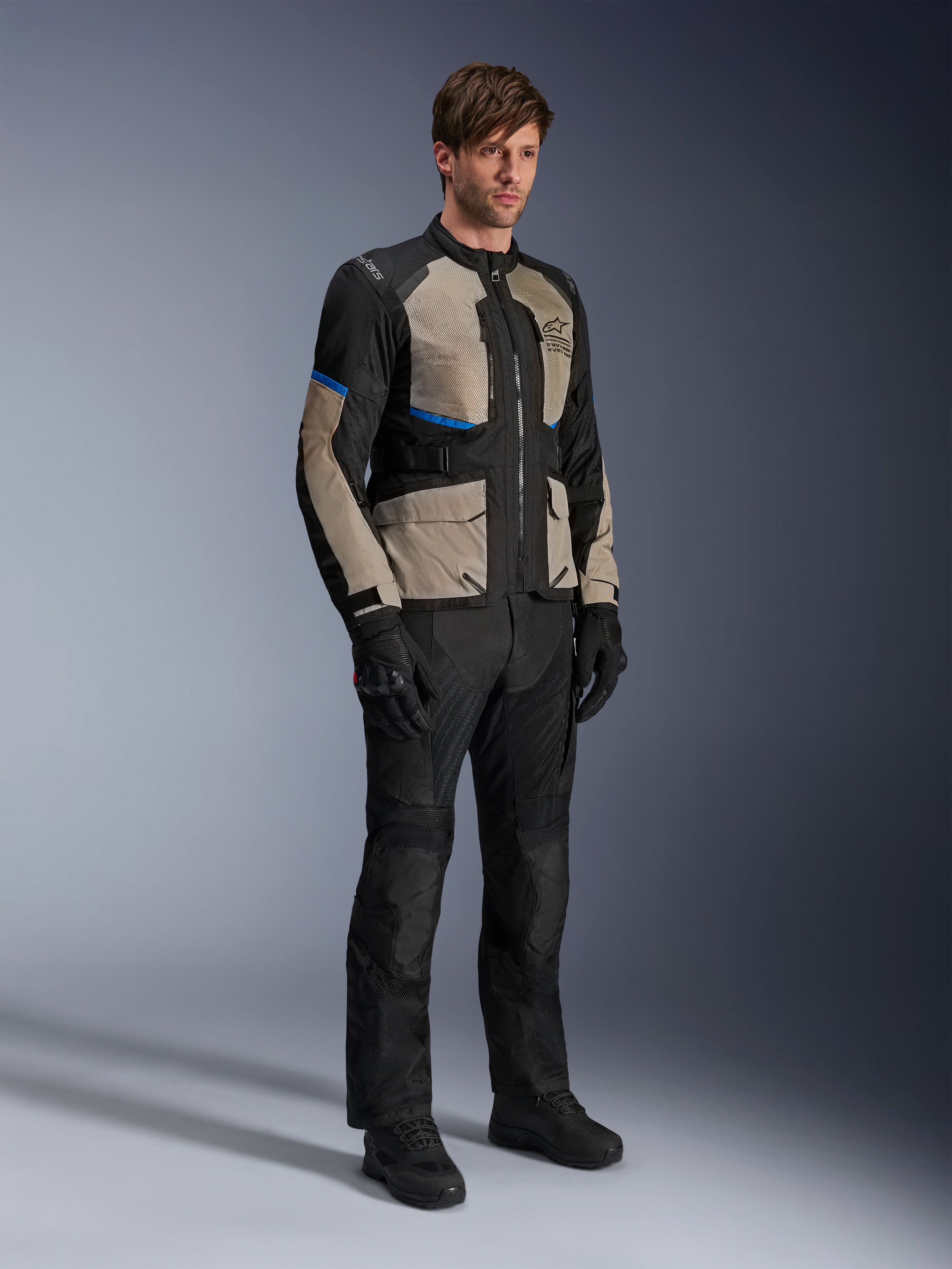 Giacca Alpinestars Andes Air Drystar®, giacca da moto touring, nero, grigio alloro e blu brillante, indossata con pantaloni e guanti da guida coordinati, dotata di ampi pannelli in rete per il flusso d'aria e vestibilità orientata alla strada, equipaggiamento adventure touring