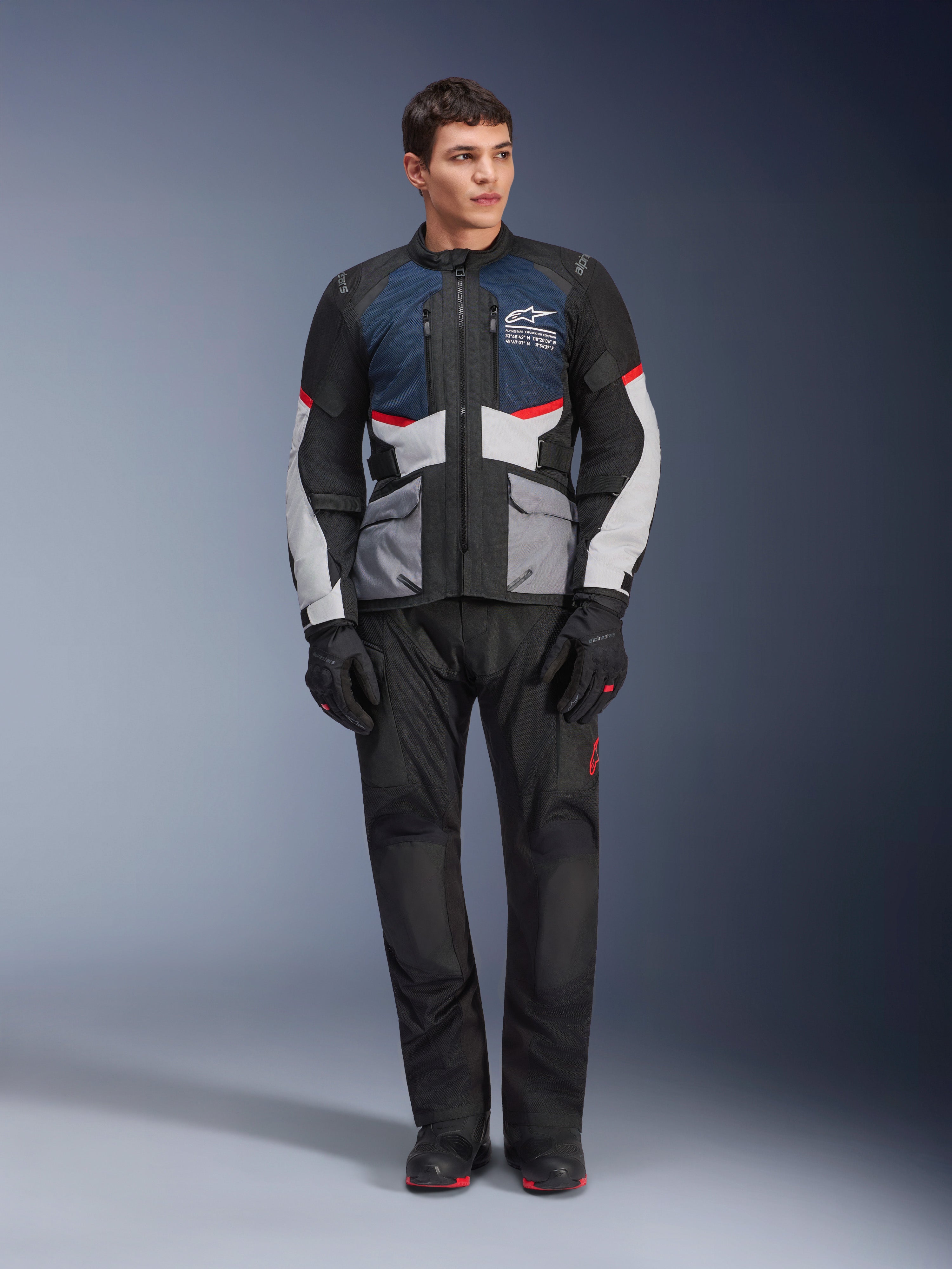 Giacca Alpinestars Andes Air Drystar®, giacca da moto touring, blu scuro, nero e grigio ghiaccio, indossata con pantaloni e guanti adventure neri coordinati, con pannelli in mesh per il flusso d'aria e un design tecnico multitasche.