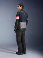 Modello uomo visto di profilo posteriore che indossa la giacca Alpinestars Andes Air Drystar® in Deep Blue Black Ice Gray, abbinata a pantaloni e guanti da moto neri, con pannello posteriore in rete blu, tasca portaoggetti grigia sulla parte bassa della schiena e accenti rossi sulle maniche, abbigliamento professionale per adventure touring.