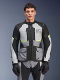 Motociclista che indossa la giacca Alpinestars Andes Air Drystar® in grigio ghiaccio, grigio scuro e nero, con accenti giallo neon e pannelli di ventilazione in rete, abbinata a pantaloni e guanti da moto coordinati, abbigliamento adventure touring