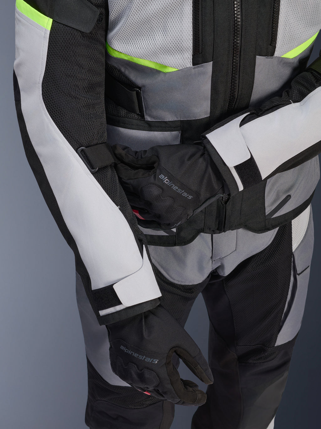Giacca Alpinestars Andes Air Drystar®, giacca da mototurismo, grigio ghiaccio e grigio scuro con dettagli giallo neon, primo piano che mostra i pannelli in rete e le cinghie di regolazione, indossata con guanti Alpinestars neri