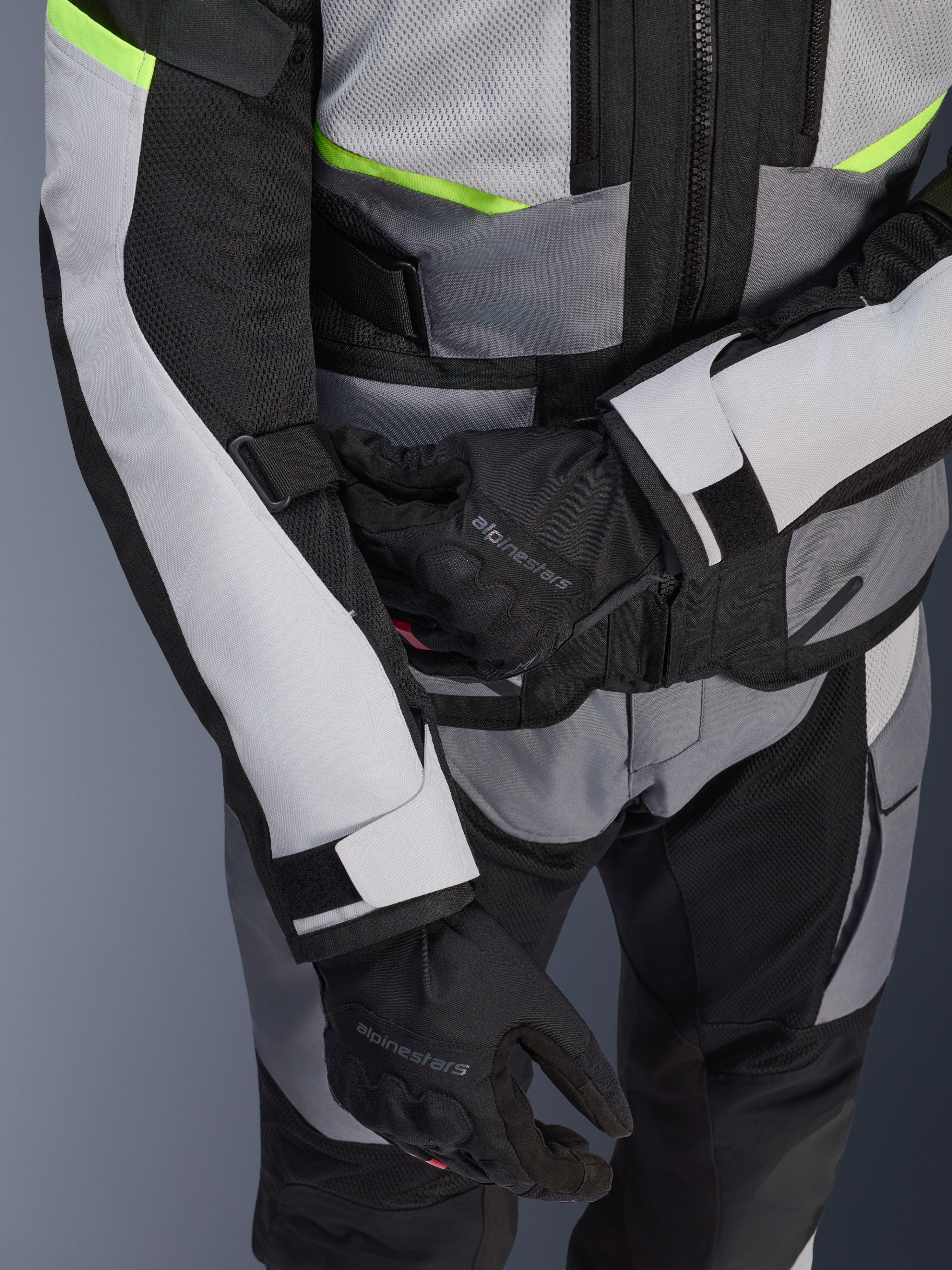 Giacca Alpinestars Andes Air Drystar®, giacca da mototurismo, grigio ghiaccio e grigio scuro con dettagli giallo neon, primo piano che mostra i pannelli in rete e le cinghie di regolazione, indossata con guanti Alpinestars neri