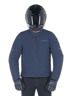 Giacca Alpinestars Husker Waterproof, Night Navy, giacca da moto urbana indossata con casco integrale nero e guanti grigi, caratterizzata da esterno in softshell tecnico e branding discreto