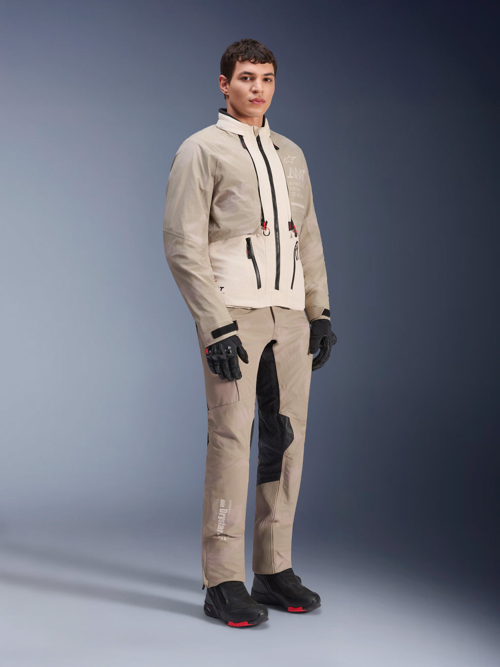 Giacca Alpinestars AMT-10LAB Drystar® XF, giacca da moto adventure, White Sand Aluminum Camo, indossata con pantaloni adventure coordinati, guanti e stivali da moto neri, inquadratura a figura intera in studio, abbigliamento protettivo multi-stagione