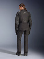 Pilota donna vista da dietro con giacca Alpinestars Stella Andes V4 Drystar®, nera, abbinata a pantaloni da moto coordinati, logo Astar bianco sulla schiena, orlo posteriore allungato, outfit completo da adventure-touring con guanti e stivali neri