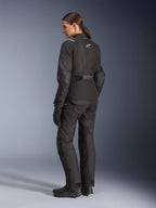 Motociclista donna che indossa la giacca Alpinestars Stella Andes V4 Drystar®, giacca da moto adventure nera, vista posteriore a 3/4, abbinata a pantaloni in tessuto e guanti coordinati, con loghi Alpinestars bianchi sulla schiena e in vita, pannelli protettivi rinforzati e orlo posteriore allungato.