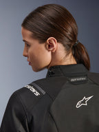Giacca Alpinestars Stella Andes V4 Drystar® da donna, nero, primo piano della parte superiore della schiena e della spalla, con logo Astar e branding ricamati in bianco, costruzione in tessuto tecnico per moto adventure