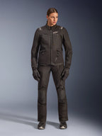 Motociclista donna che indossa la giacca Alpinestars Stella Andes V4 Drystar® in nero, abbinata a pantaloni e guanti adventure-touring coordinati neri, caratterizzata da una costruzione in tessuto tecnico con molteplici tasche multiuso e loghi Alpinestars bianchi, abbigliamento da moto completo per ogni condizione atmosferica