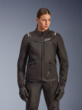 Alpinestars Stella Andes V4 Drystar Jacket, giacca da moto touring da donna, nera, indossata da una modella con pantaloni da moto e guanti coordinati, con chiusura frontale con zip, logo bianco sul petto e branding Alpinestars sulle spalle, abbigliamento tecnico per ogni condizione climatica.