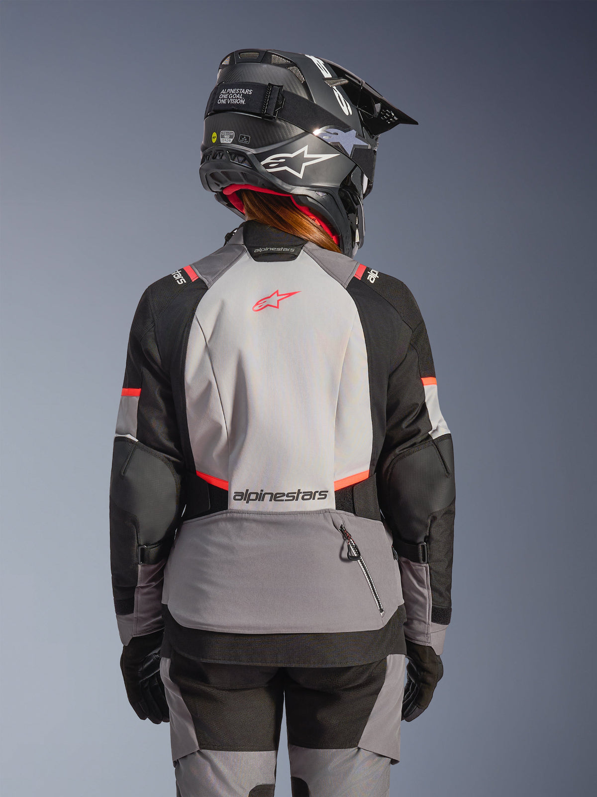 Alpinestars giacca Stella Andes V4 Drystar®, giacca da moto touring adventure da donna, grigia e nera con dettagli corallo fluo, vista posteriore su modella con casco.