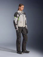Giacca Alpinestars Stella Andes V4 Drystar® da donna, grigio ghiaccio, grigio scuro e nero con dettagli giallo fluo, indossata da una modella con pantaloni da moto e guanti neri, abbigliamento protettivo da adventure touring per donna