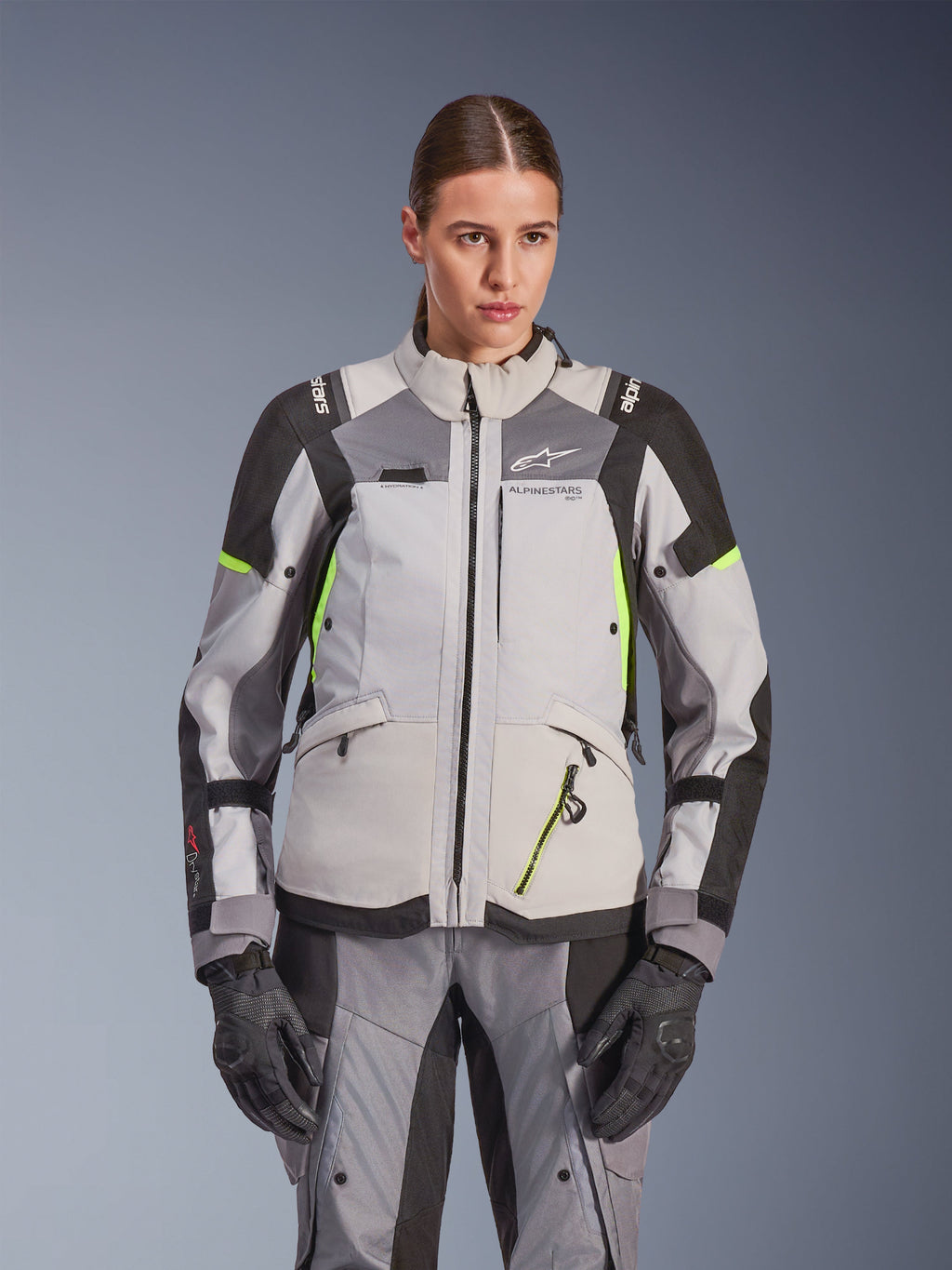 Giacca da donna Alpinestars Stella Andes V4 Drystar®, grigio ghiaccio e grigio scuro con accenti giallo fluo, giacca da moto adventure touring, indossata con pantaloni e guanti abbinati, caratterizzata da una costruzione tessile protettiva e branding Alpinestars.