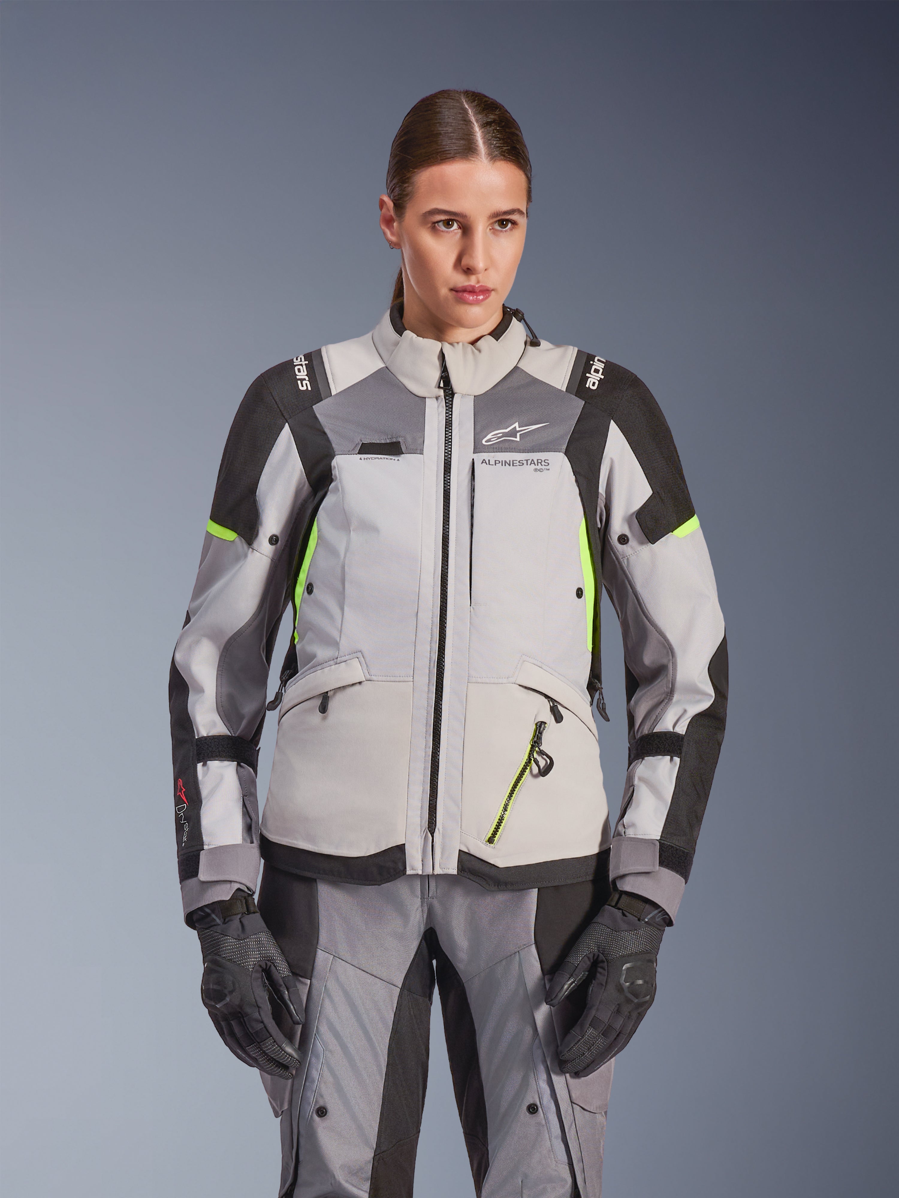Giacca da donna Alpinestars Stella Andes V4 Drystar®, grigio ghiaccio e grigio scuro con accenti giallo fluo, giacca da moto adventure touring, indossata con pantaloni e guanti abbinati, caratterizzata da una costruzione tessile protettiva e branding Alpinestars.