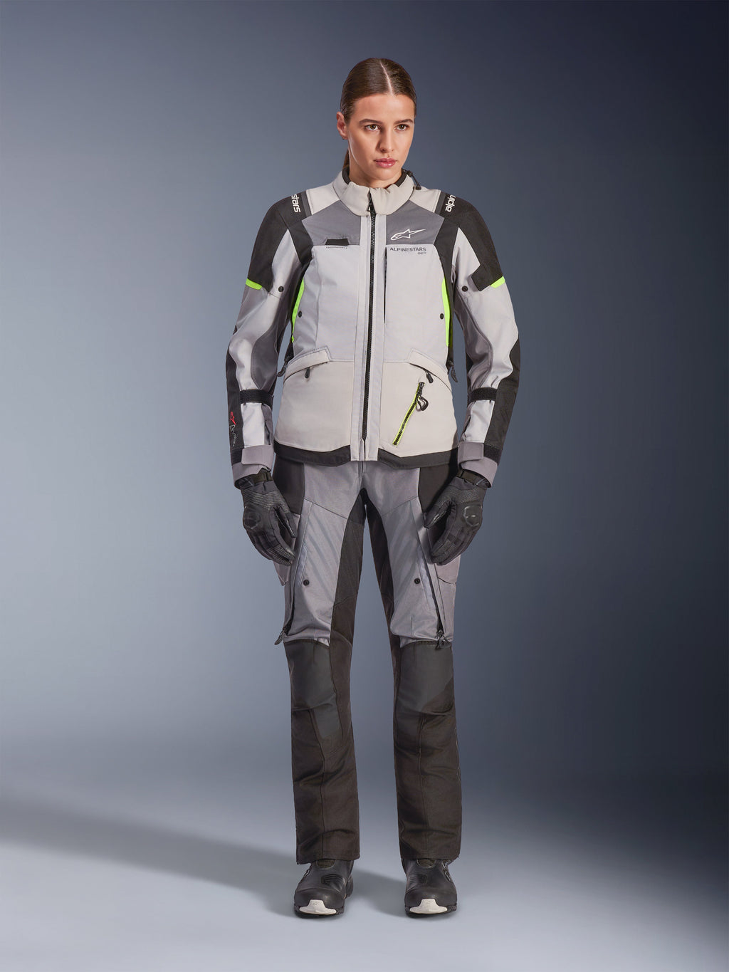 Giacca Alpinestars Stella Andes V4 Drystar® da donna, grigio ghiaccio e grigio scuro con dettagli neri e giallo fluo, indossata con pantaloni e guanti coordinati, abbigliamento adventure-touring impermeabile per donna