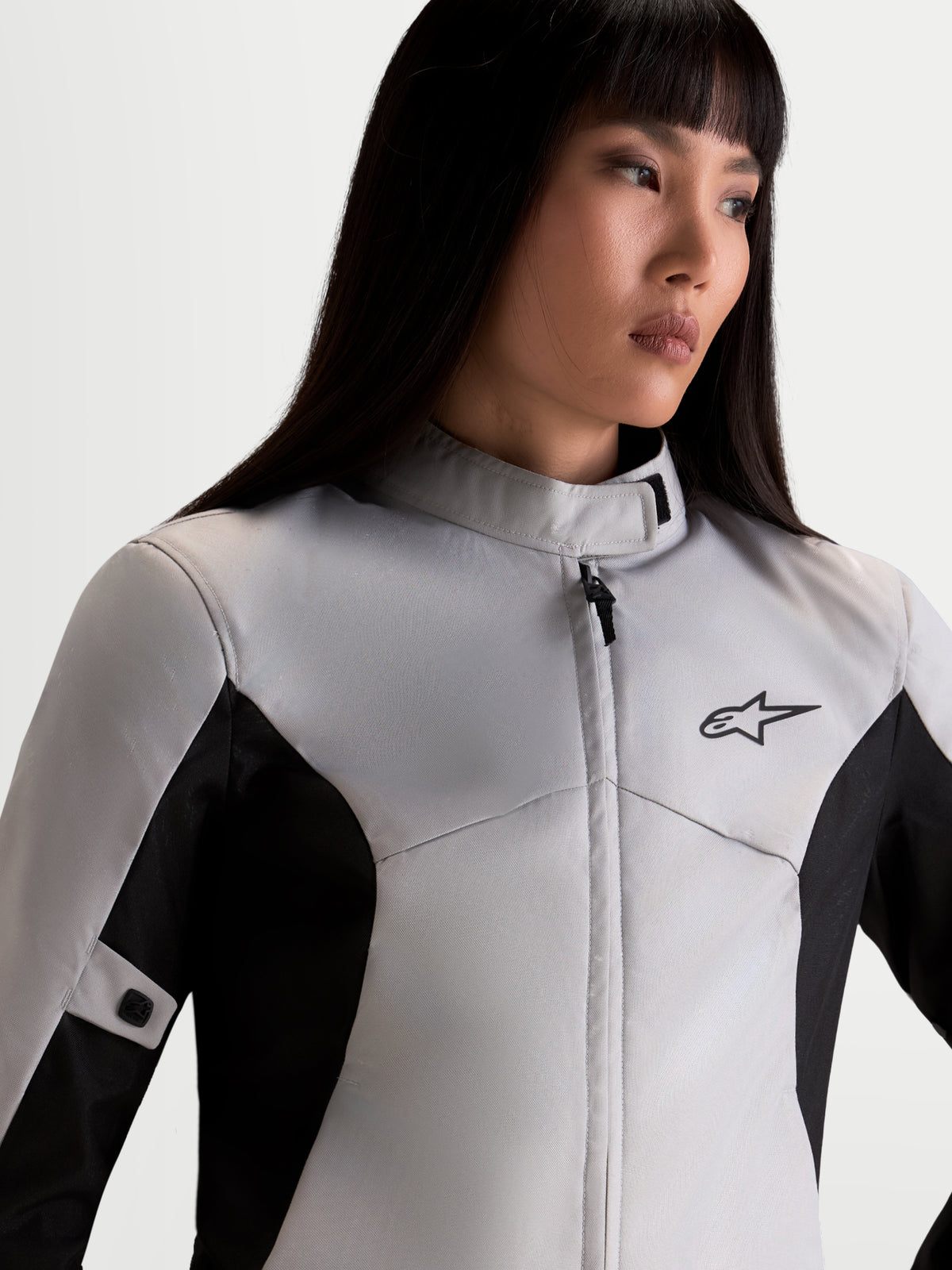 Alpinestars Stella C-1 Waterproof Giacca, giacca da moto urbana da donna in grigio ghiaccio e nero, primo piano della parte superiore del corpo che mostra il collo alto, la struttura in tessuto impermeabile e il logo A-star indossata da una modella