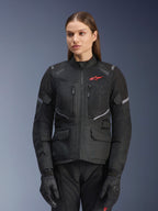 Alpinestars Stella Andes Air Drystar Jacket, giacca da moto touring da donna, nera con dettagli grigi e un piccolo logo rosso, con pannelli di ventilazione in rete, collo alto e diverse tasche utility, indossata con guanti e pantaloni coordinati