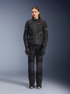 Modella che indossa la giacca Alpinestars Stella Andes Air Drystar® in nero, abbinata a pantaloni da touring e guanti neri coordinati, con ampi pannelli di ventilazione in rete, dettagli del logo in rosso e inserti riflettenti, scatto professionale in studio per abbigliamento da moto da donna.