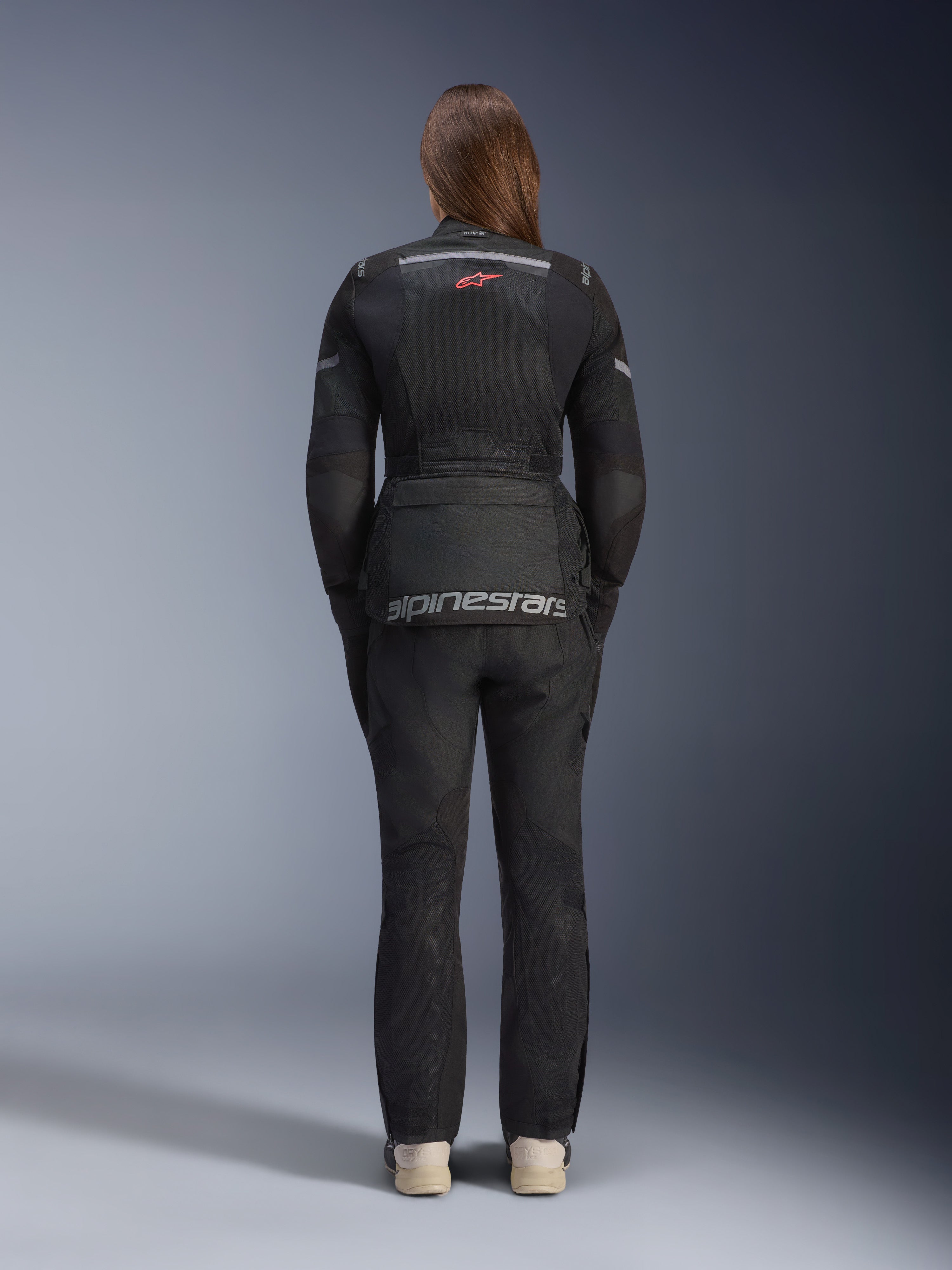 Donna che indossa la giacca Alpinestars Stella Andes Air Drystar® e pantaloni abbinati, nero, vista posteriore con grande branding Alpinestars grigio sulla tasca posteriore, piccolo logo a stella rosso, pannelli di ventilazione in rete e dettagli riflettenti per adventure touring