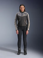 Donna che indossa la giacca Alpinestars Stella T-Dyno WR, Nero Grigio Scuro ed Ecru, vista frontale, giacca da moto in tessuto dal design d'ispirazione vintage, con logo su petto e maniche, indossata con pantaloni e stivali neri