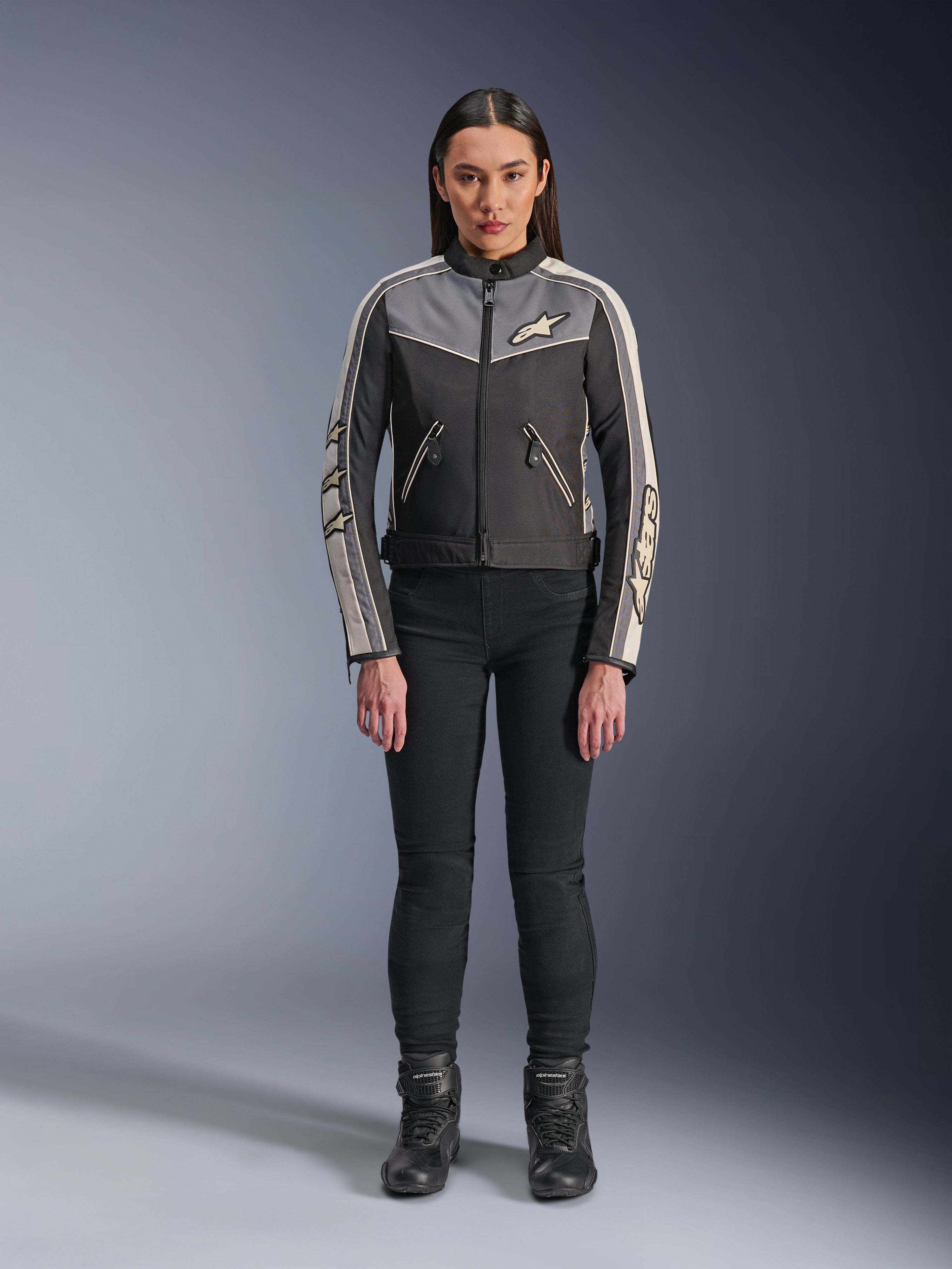 Donna che indossa la giacca Alpinestars Stella T-Dyno WR, Nero Grigio Scuro ed Ecru, vista frontale, giacca da moto in tessuto dal design d'ispirazione vintage, con logo su petto e maniche, indossata con pantaloni e stivali neri