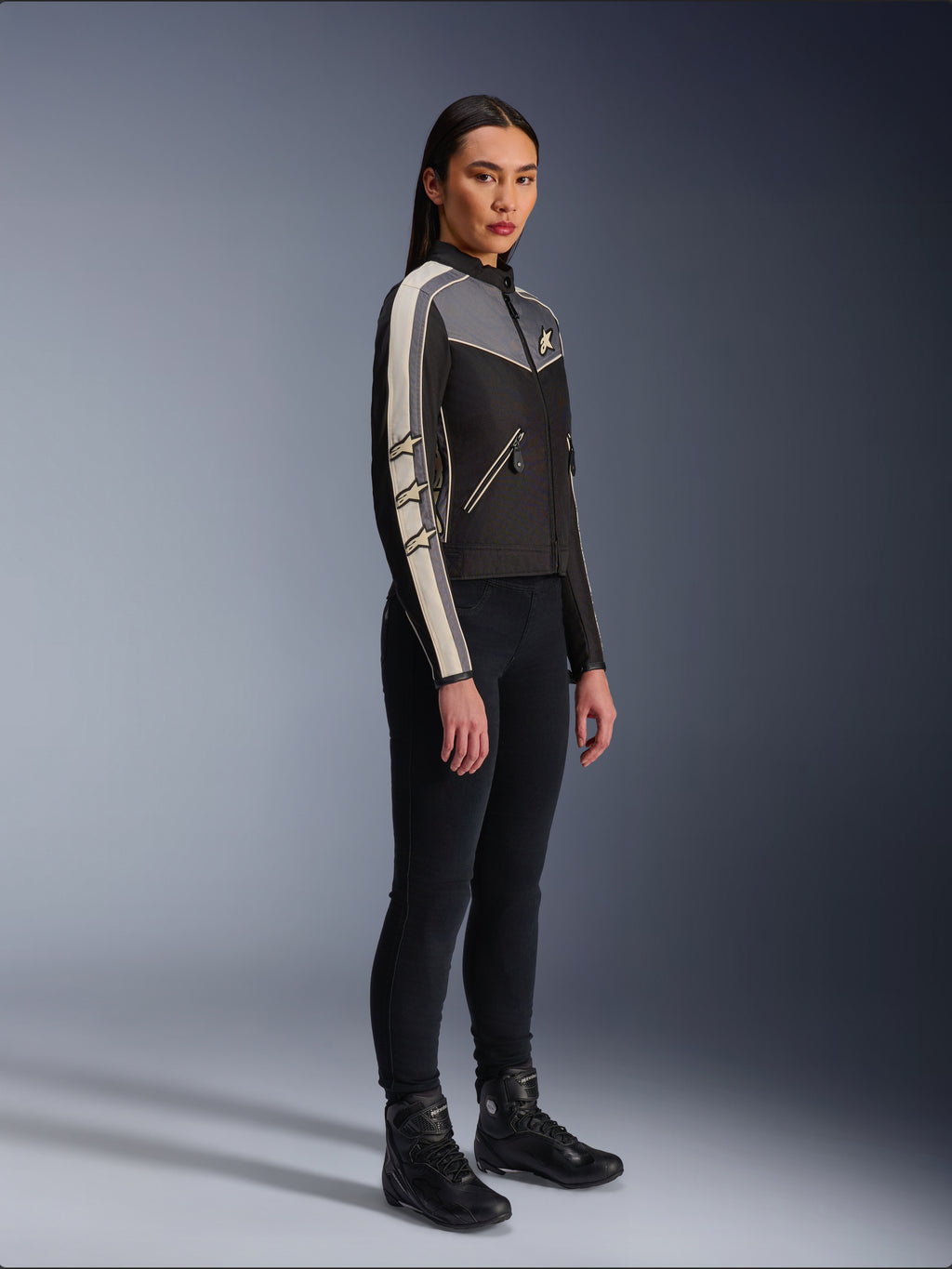 Giacca Alpinestars Stella T-Dyno WR, giacca da moto in tessuto da donna, nero, grigio scuro ed ecru, design d'ispirazione vintage con strisce sulle maniche color panna e loghi a stella, indossata con pantaloni neri e stivali da moto, abbigliamento urban riding d'ispirazione heritage