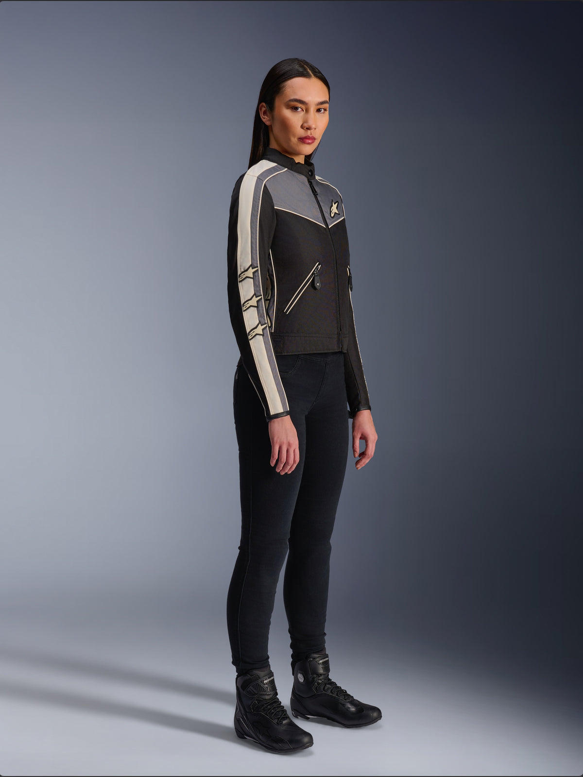 Giacca Alpinestars Stella T-Dyno WR, giacca da moto in tessuto da donna, nero, grigio scuro ed ecru, design d'ispirazione vintage con strisce sulle maniche color panna e loghi a stella, indossata con pantaloni neri e stivali da moto, abbigliamento urban riding d'ispirazione heritage