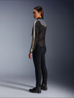 Modella vista di profilo e da dietro che indossa la giacca Alpinestars Stella T-Dyno WR in Nero Grigio Scuro Ecru, caratterizzata da un design di ispirazione vintage con strisce sulle maniche color ecru e un inserto posteriore grigio, abbinata a pantaloni neri e scarpe da moto nere.