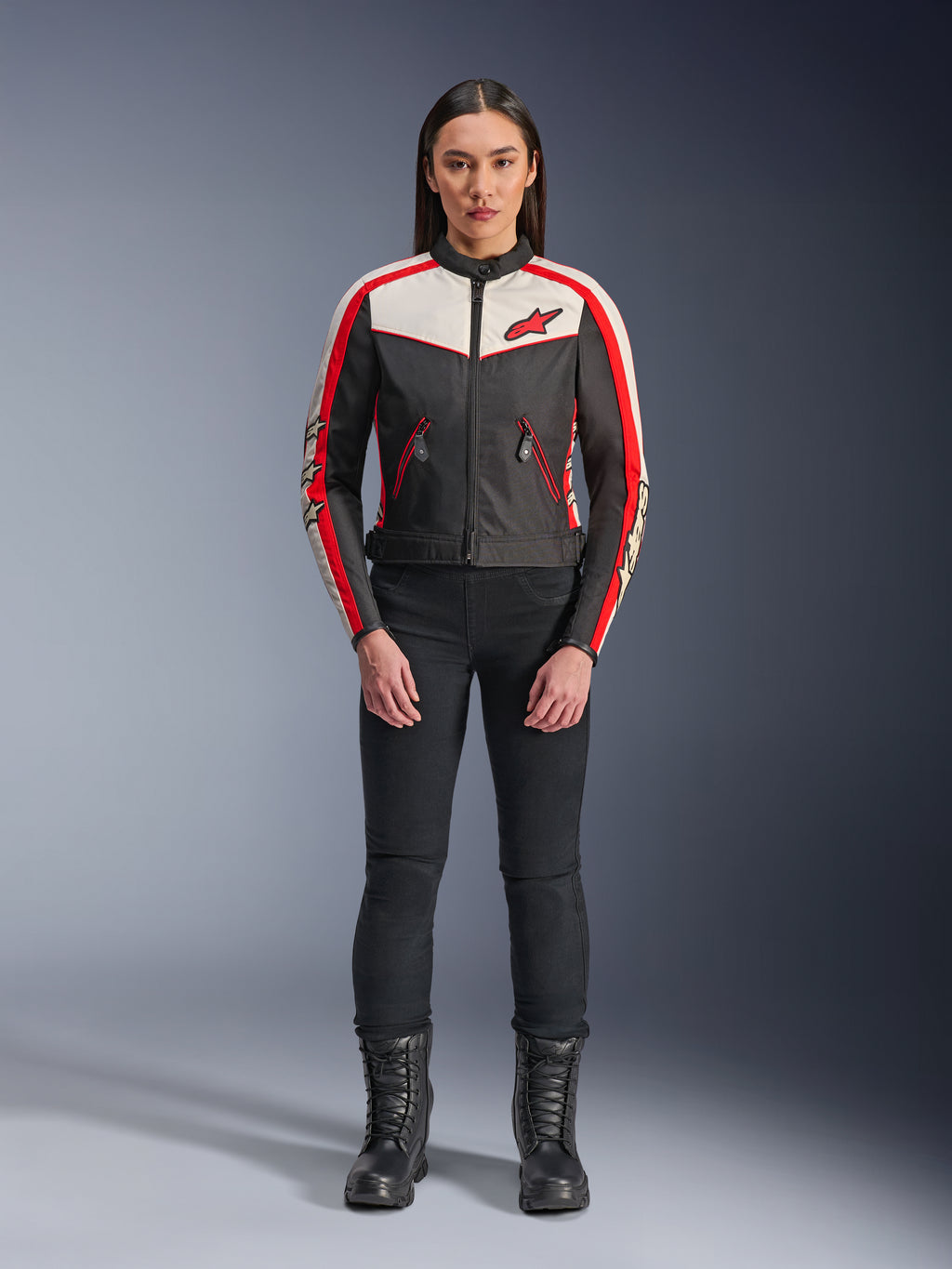 Giacca Alpinestars Stella T-Dyno WR, giacca da moto in tessuto da donna, nero, ecru e rosso acceso, indossata da una modella con pantaloni e stivali neri, caratterizzata da un design d'ispirazione vintage con logo Alpinestars rosso e pannelli a contrasto.