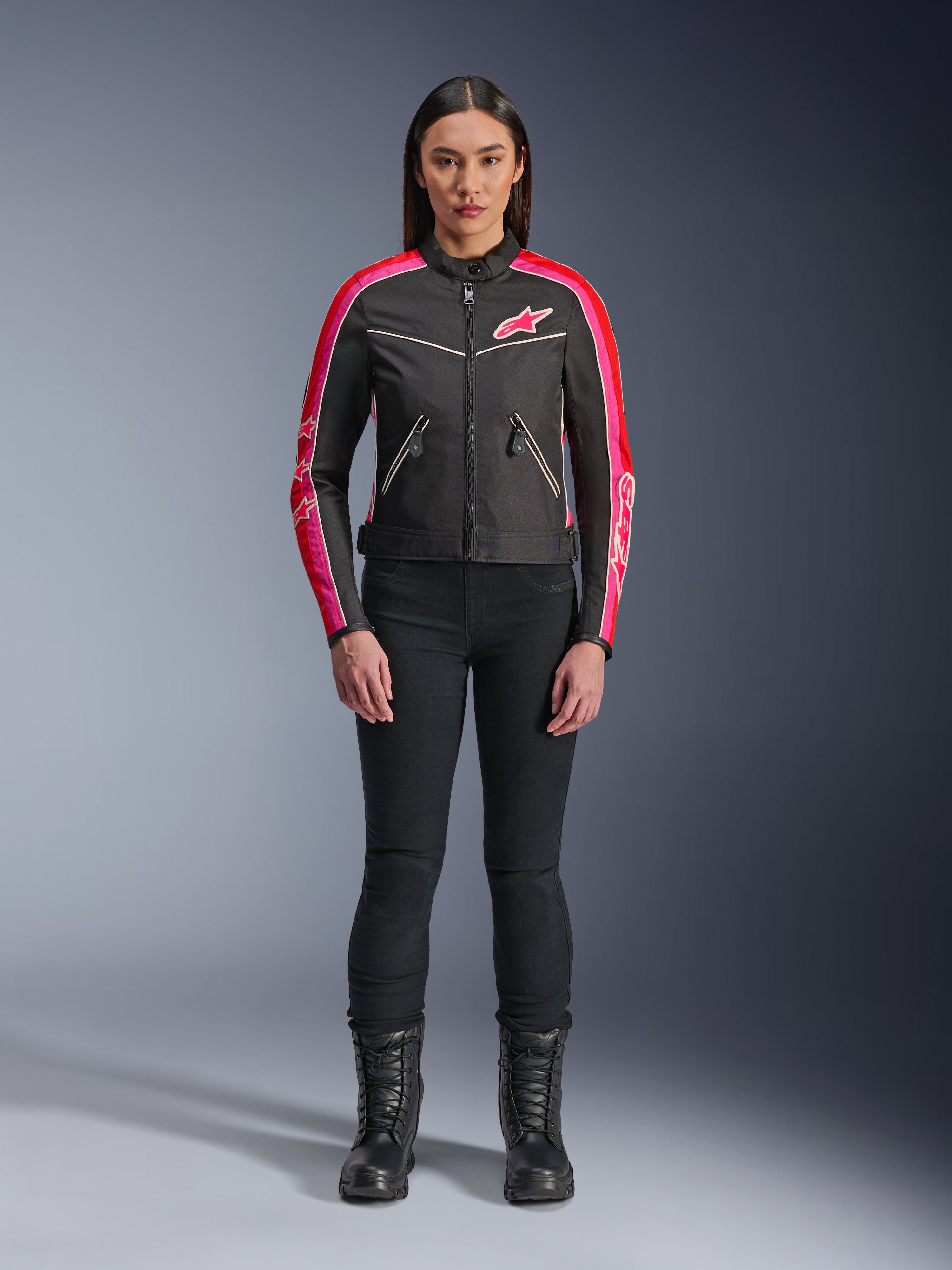 Giacca Alpinestars Stella T-Dyno WR, giacca in tessuto stile vintage, nero con accenti rosso brillante e fucsia, logo rosa e strisce sulle maniche, indossata con pantaloni neri e stivali stringati, abbigliamento da moto urban