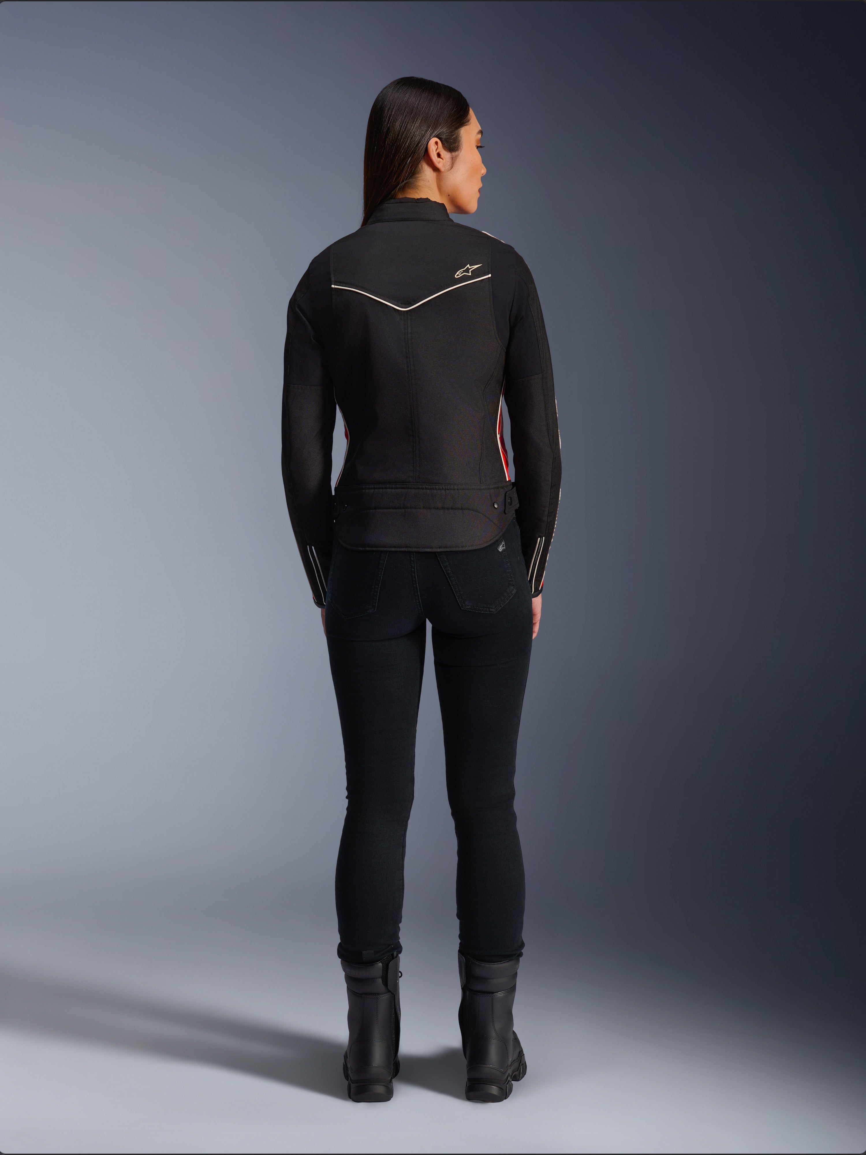 Modella vista da dietro con giacca Alpinestars Stella T-Dyno WR in Nero Rosso Brillante Fucsia, giacca da moto in tessuto con vestibilità da biker più corta, vista posteriore che mostra il logo a stella bianco, abbinata a pantaloni neri e stivali neri