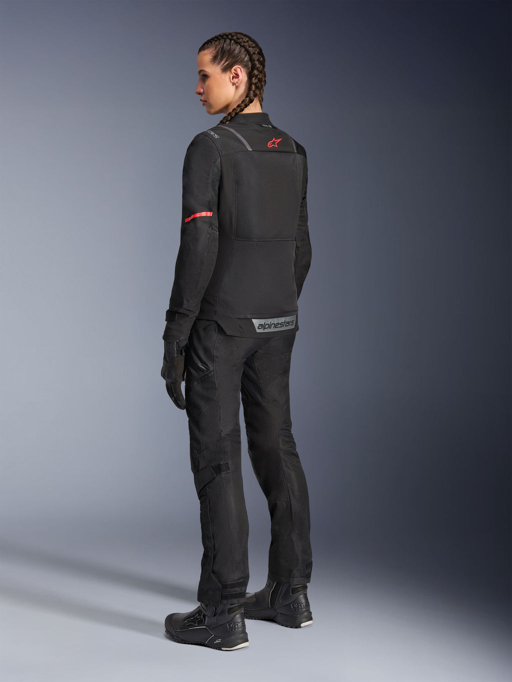 Giacca Alpinestars Stella ST-2 Air, giacca da moto da donna, nera con dettagli rossi su maniche e schiena, vista posteriore su modella con pantaloni e stivali coordinati, logo riflettente e struttura in tessuto moderno.
