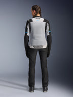 Alpinestars Stella ST-2 Air Jacket, Ice Gray Black, vista posteriore su modella, con ampio pannello posteriore in rete grigio chiaro, maniche nere con strisce blu, logo Alpinestars sulla parte bassa della schiena, abbinata a pantaloni tecnici e stivali neri, abbigliamento touring estivo
