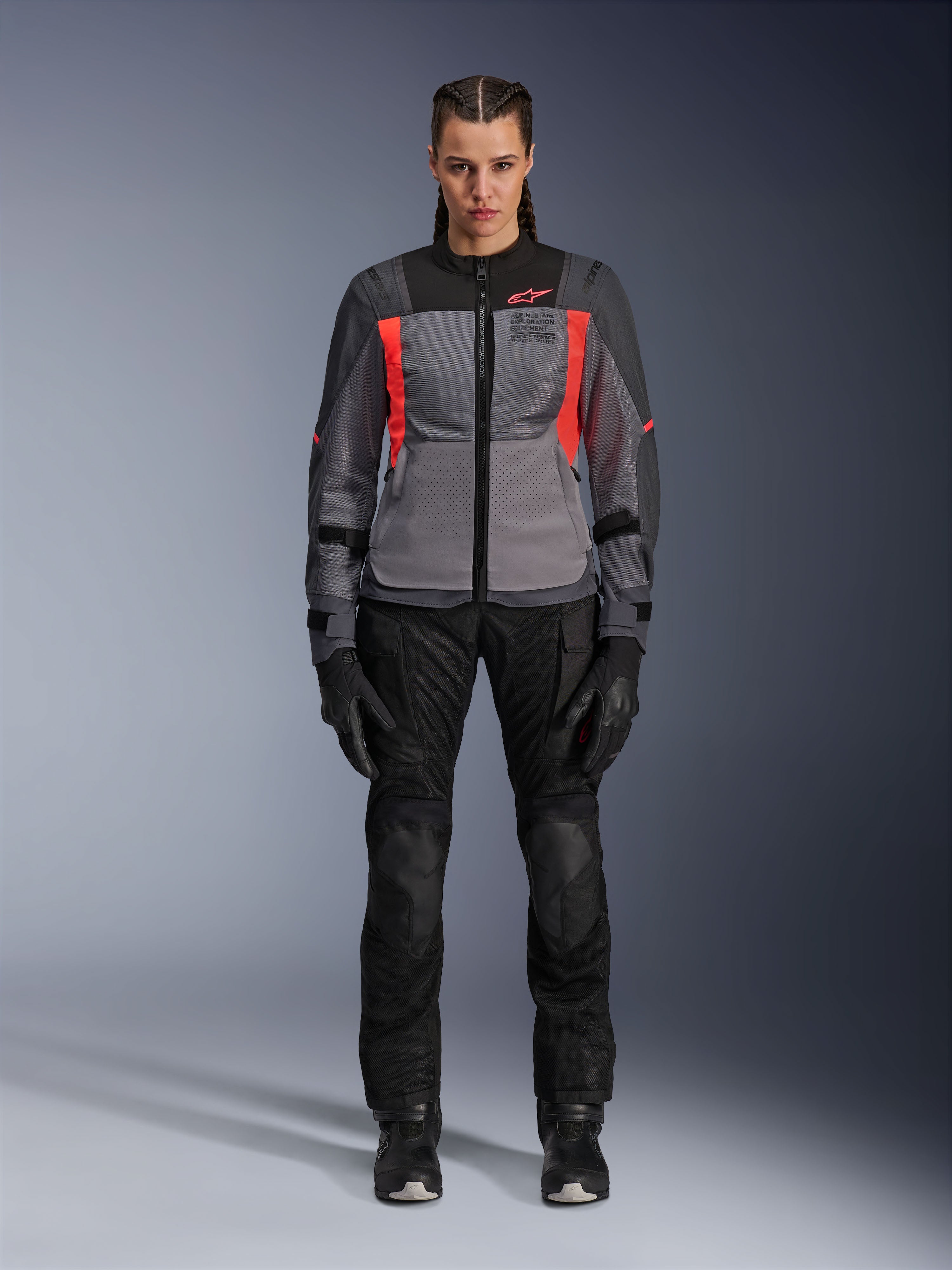 Donna che indossa la giacca Alpinestars Stella ST-2 Air in Deep Gray, Dark Gray e Fluo Coral, abbinata a pantaloni e guanti da moto neri, vista frontale, abbigliamento da adventure touring moderno in rete per donna