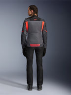Vista posteriore di una modella che indossa la giacca Alpinestars Stella St-2 Air da donna in Deep Gray e Dark Gray con accenti Fluo Coral, con ampi pannelli di ventilazione in mesh sulla schiena e dettagli del logo riflettenti, abbinata a pantaloni e guanti da moto neri.