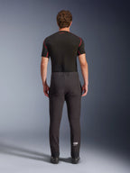 Pantaloni Alpinestars Aeroshell, pantaloni da moto crossover sportivi in softshell, nero, vista posteriore indossati con uno strato base nero a maniche corte, caratterizzati da vestibilità slim, ginocchia pre-curvate e logo Astars bianco sulla parte inferiore della gamba sinistra.