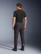 Pantaloni Alpinestars Aeroshell, nero, pantaloni da moto in softshell, vista posteriore su un modello, caratterizzati da un taglio moderno affusolato, logo Astars bianco sulla parte inferiore della gamba e orli elasticizzati, indossati con un base layer nero a maniche corte e scarpe da moto.