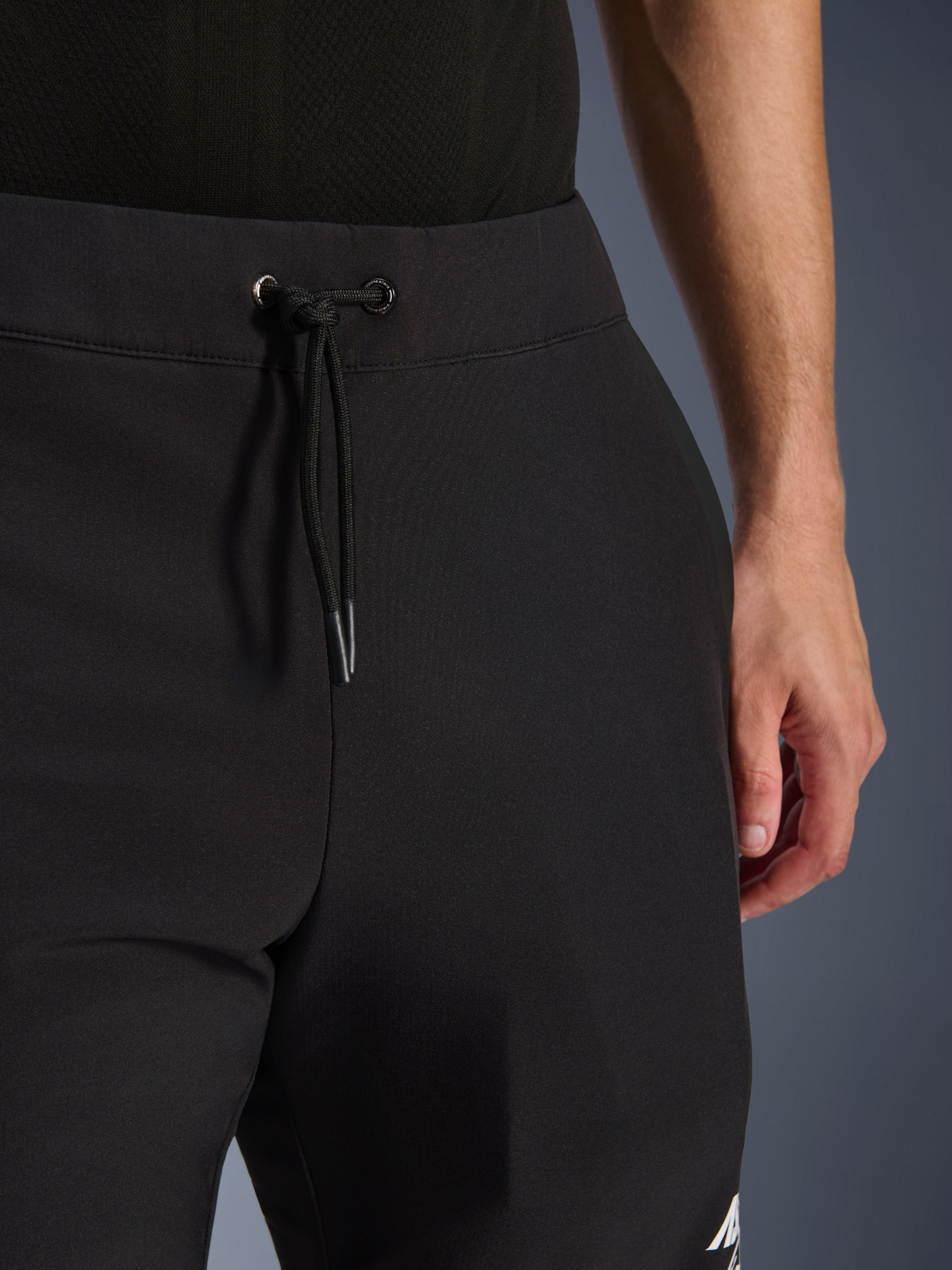 Pantaloni Alpinestars Aeroshell, pantaloni da moto in softshell nero, vista ravvicinata della vita elastica e della chiusura con cordoncino, design moderno e minimalista, costruzione in tessuto resistente per il touring casual