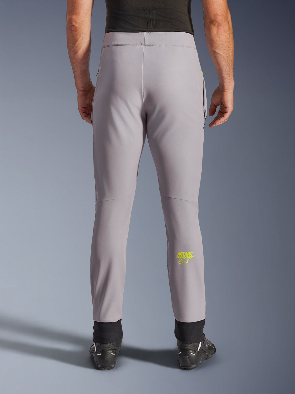 Pantaloni Alpinestars Aeroshell, pantaloni da moto, grigio medio e giallo fluo, vista posteriore con logo Astars giallo sul polpaccio, polsini elastici neri alle caviglie, design moderno in tessuto softshell per guida su strada e casual