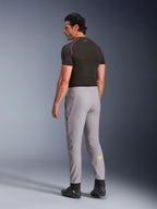 Alpinestars Pantaloni Aeroshell, Mid Gray Yellow Fluo, vista posteriore di un modello che indossa pantaloni da moto in softshell elasticizzato, logo Astars giallo sul polpaccio sinistro, abbinati a un base layer nero e scarpe tecniche per una silhouette sportiva moderna.