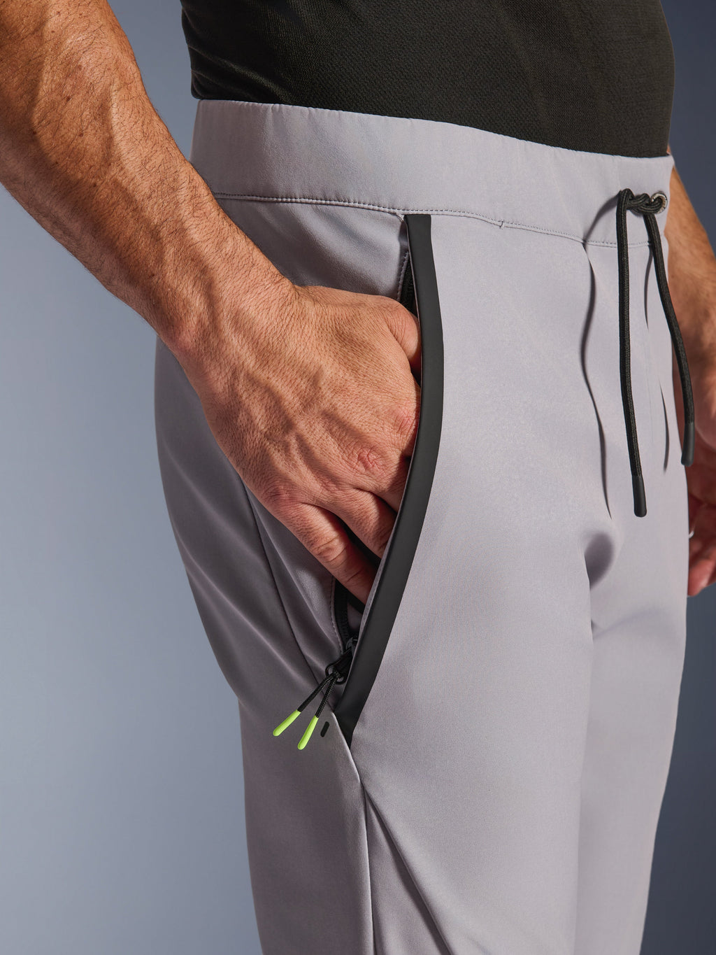 Alpinestars Aeroshell Pants, pantaloni da moto crossover in softshell, grigio medio e giallo fluo, primo piano della tasca anteriore con zip e della vita, cerniera nera nastrata con terminali giallo fluo, vita elastica con coulisse nera