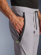 Alpinestars Aeroshell Pants, pantaloni da moto crossover in softshell, grigio medio e giallo fluo, primo piano della tasca anteriore con zip e della vita, cerniera nera nastrata con terminali giallo fluo, vita elastica con coulisse nera