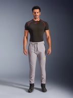 Modello maschile che indossa pantaloni Alpinestars Aeroshell in Grigio Medio e Giallo Fluo, pantaloni softshell sportivi crossover con vita elastica a cordoncino e tasche con zip, abbinati a una maglia tecnica nera a maniche corte, design atletico moderno per la guida su strada e casual