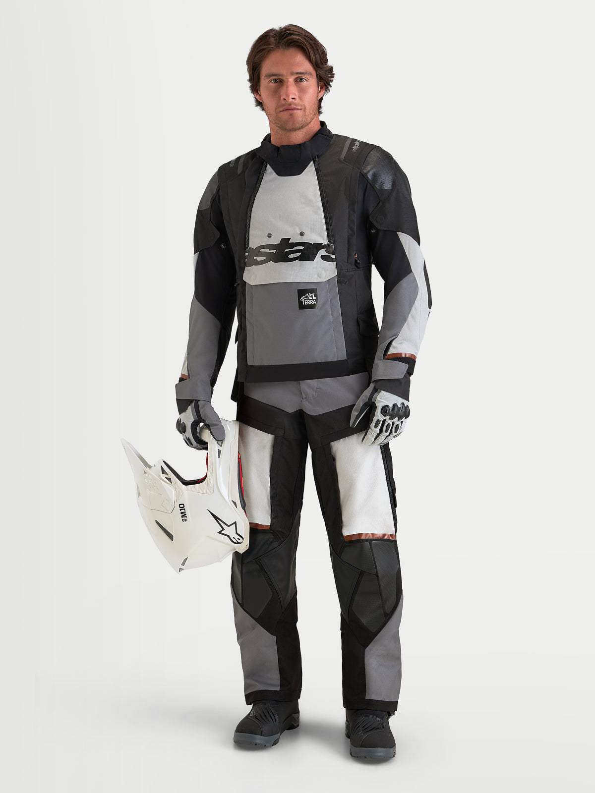 Alpinestars Harok V 2 Pantaloni Drystar, pantaloni da moto adventure da uomo in grigio scuro, grigio ghiaccio e nero, indossati da un modello con giacca ADV coordinata che tiene un casco bianco
