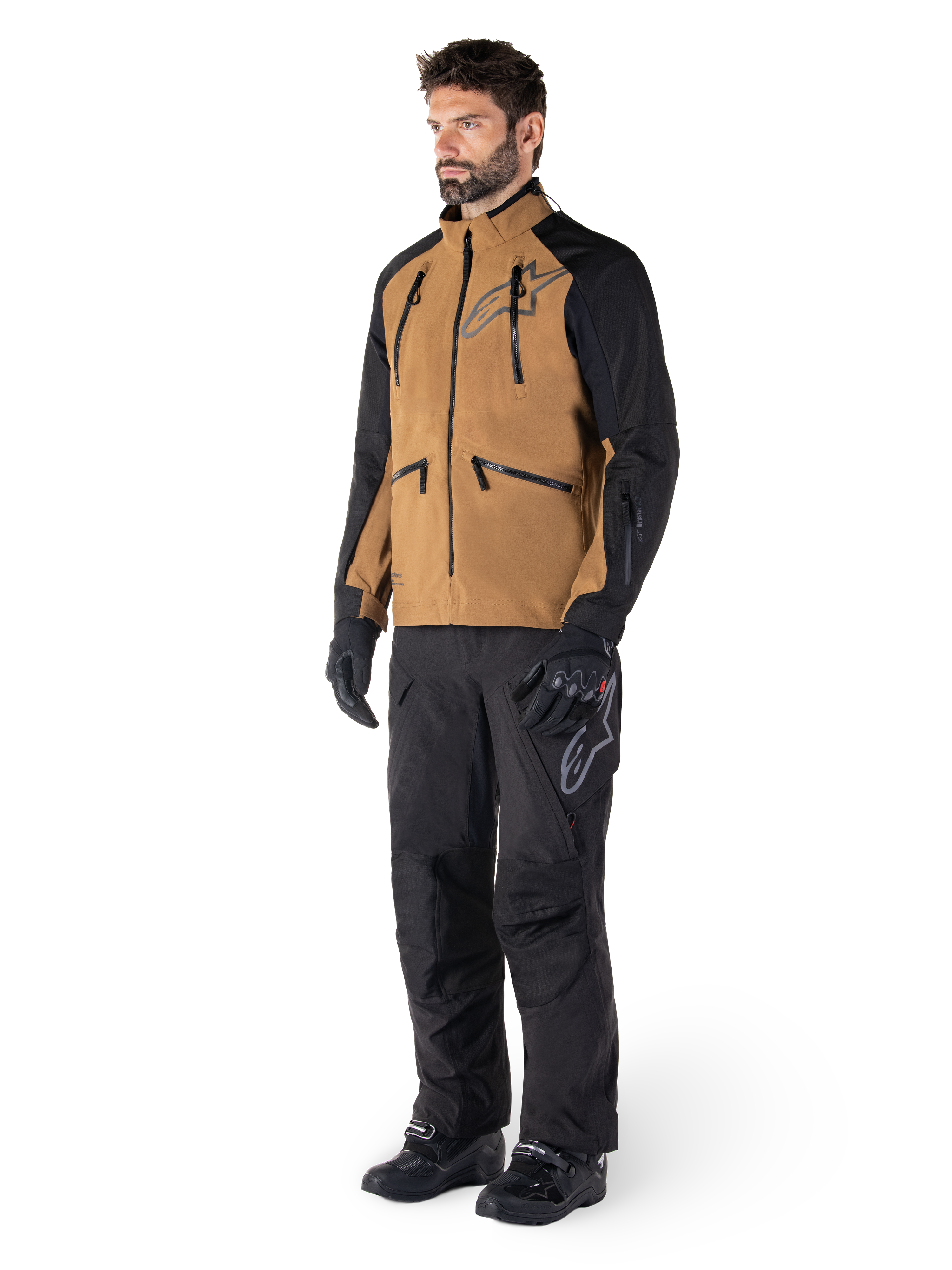 Alpinestars Hyde XT Drystar® Pants, pantaloni da moto adventure, nero, indossati con giacca tecnica marrone e nera, guanti e stivali neri, caratterizzati da un design sopra lo stivale per la guida off-road e dual-sport