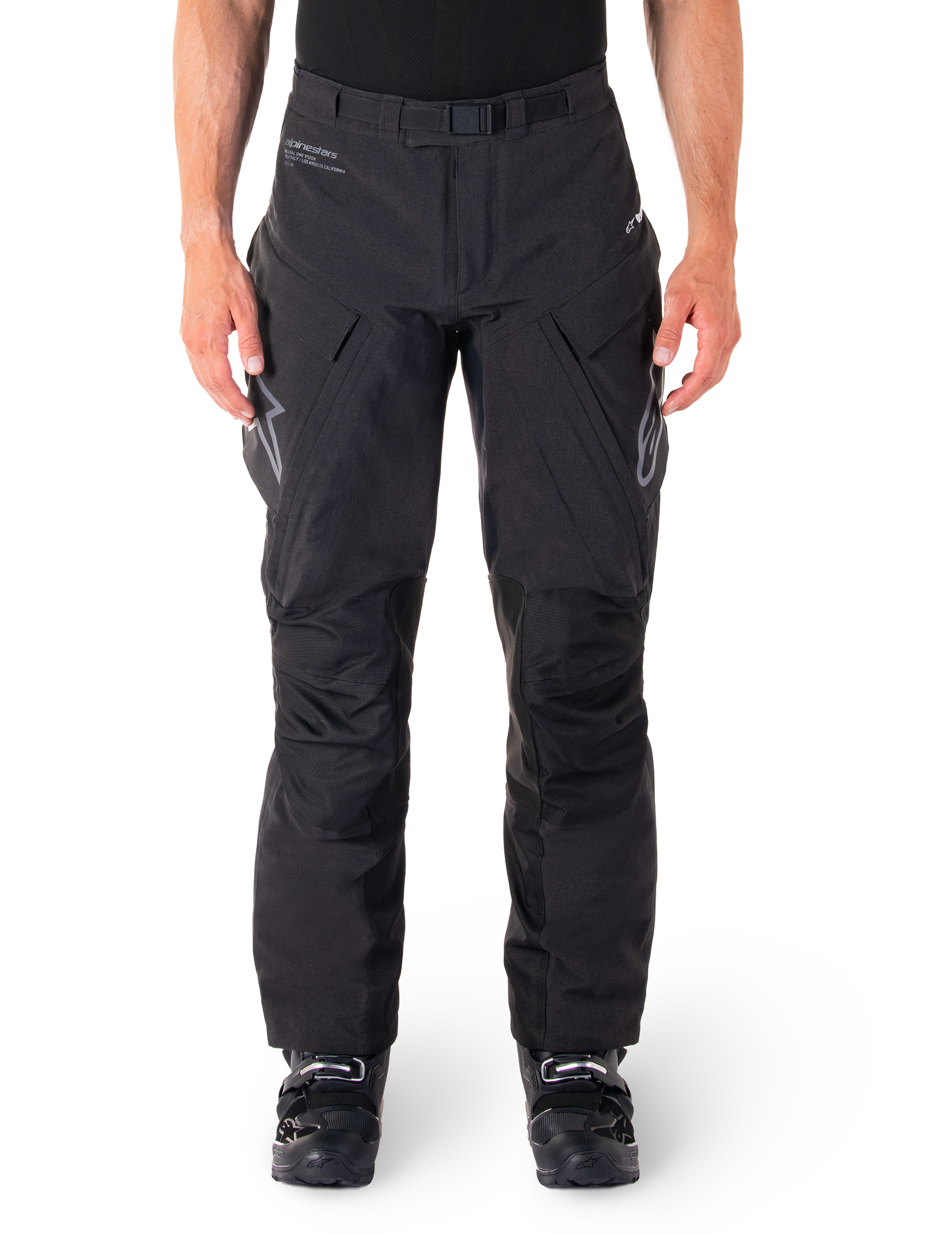 Pantaloni Alpinestars Hyde XT Drystar, pantaloni adventure touring neri, indossati da un pilota con stivali neri, con loghi grigi sulle cosce, cintura integrata, pannelli rinforzati sulle ginocchia e costruzione in tessuto impermeabile
