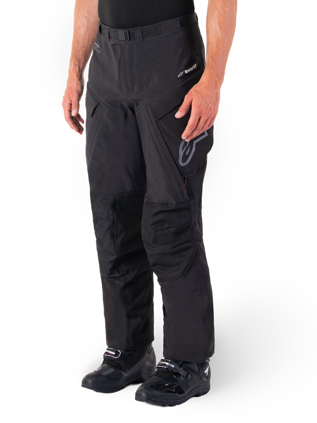Alpinestars Hyde XT Drystar® Pants, pantaloni da moto adventure touring, nero, indossati con stivali neri, con logo della membrana laminata Drystar®XF, pannelli rinforzati sulle ginocchia e tasche cargo con zip