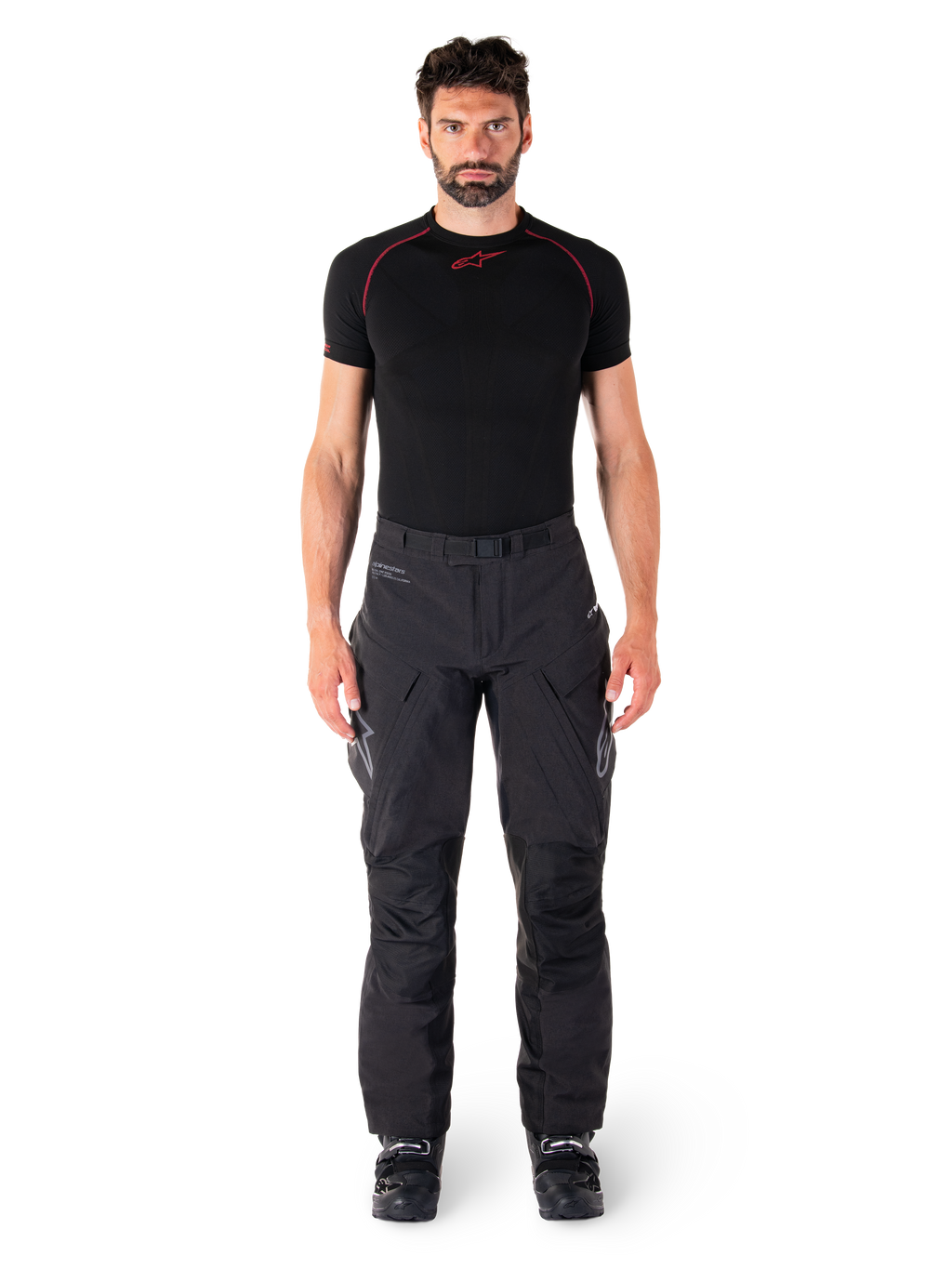 Pantaloni Alpinestars Hyde XT Drystar®, pantaloni da moto adventure touring, nero, indossati da un modello con base layer nero a maniche corte e stivali neri, caratterizzati da materiale tecnico elasticizzato, pannelli rinforzati sulle ginocchia e tasche cargo ergonomiche