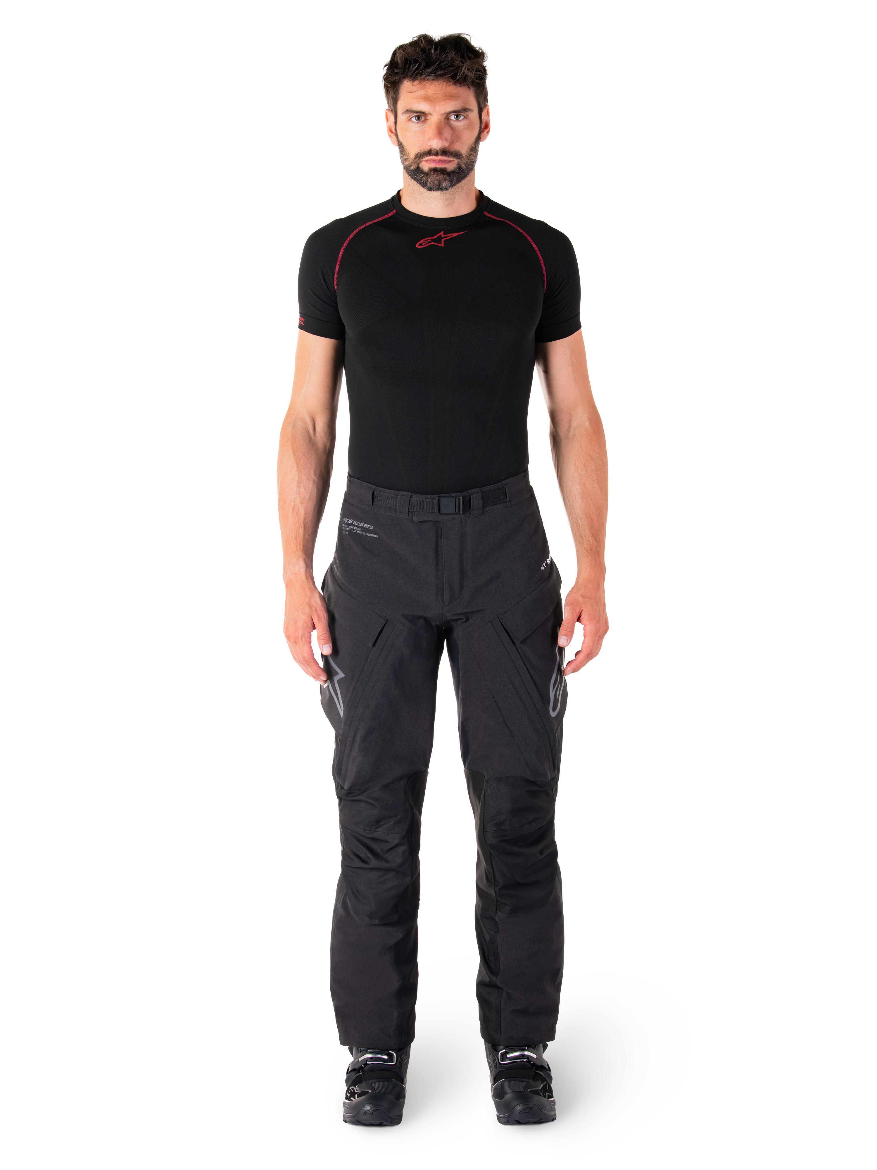 Pantaloni Alpinestars Hyde XT Drystar®, pantaloni da moto adventure touring, nero, indossati da un modello con base layer nero a maniche corte e stivali neri, caratterizzati da materiale tecnico elasticizzato, pannelli rinforzati sulle ginocchia e tasche cargo ergonomiche